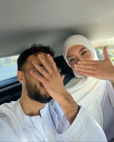 a woman covering her face while sitting in a car with a man holding his hand up