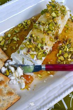 a white plate topped with cheese and nuts next to crackers on top of a table