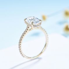 a close up view of a diamond ring on a white surface with flowers in the background