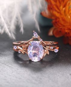 Step into a world of timeless elegance with our Vintage Oval Cut Lavender Amethyst Engagement Ring set in rose gold, a captivating testament to nature's beauty and vintage charm. This exquisite ring features an oval-cut lavender amethyst as its centerpiece, exuding a soft, ethereal allure that is both captivating and enchanting. Surrounding the lavender amethyst are delicate clusters of moss agate gemstones, intricately arranged in an art deco-inspired leaf motif. This nature-inspired design add Elegant Lavender Rings For Wedding, Elegant Lavender Wedding Rings, Oval Lavender Rings For Wedding, Lavender Oval Wedding Ring, Delicate Lavender Jewelry For Wedding, Delicate Lavender Wedding Jewelry, Rose Gold Art, Amethyst Engagement Ring, Lavender Amethyst