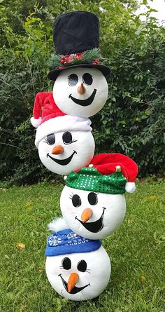 three snowmen with hats and scarfs on their heads are standing in the grass