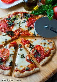 a sliced pizza on a cutting board next to some tomatoes and basil leaves, with a slice being taken out of the pizza