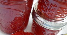 two jars filled with raspberry jam next to a spoon