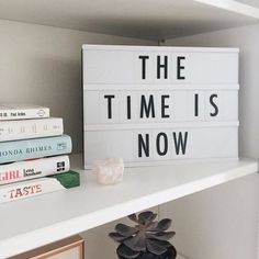 a white shelf topped with books and a sign that says the time is now on it