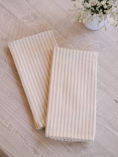 two folded towels sitting on top of a wooden table next to a vase with flowers