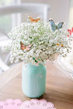 a vase filled with white flowers and butterflies on top of a wooden table next to a doily