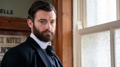 a man with a beard standing in front of a window