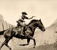 a man riding on the back of a brown horse next to a rocky mountain range