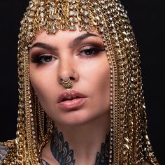 a close up of a woman with tattoos and gold chains on her face, wearing a headdress