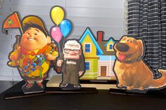 three paper cutouts of cartoon characters and a dog on a table with balloons in the background