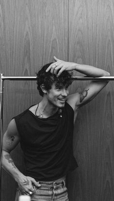 black and white photograph of a man with tattoos on his arm, leaning against a wall