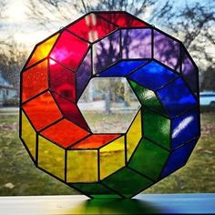 a multi - colored stained glass sculpture sitting on top of a window sill in front of a tree