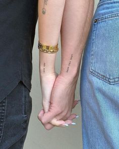 two people holding hands with tattoos on their arms and one has a gold chain around the wrist