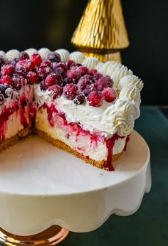 a cheesecake with berries and whipped cream is on a cake stand next to a gold lamp