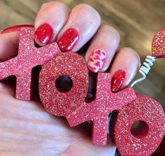 a woman's hand with red and pink nail polish holding up the word love