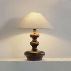 a lamp sitting on top of a table next to a white wall with a light on it