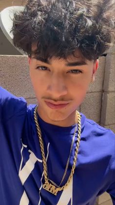 a young man with curly hair wearing a blue shirt and gold chain around his neck