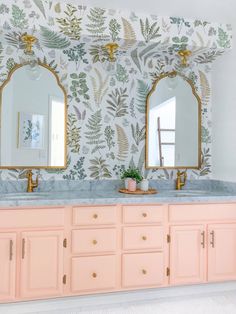 a bathroom with two sinks and mirrors on top of the countertop, in front of a floral wallpaper