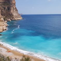 a beach with blue water and cliffs in the background