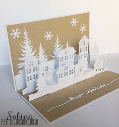 a paper cut christmas card with white houses and trees