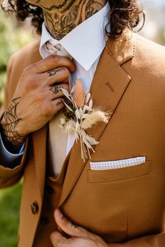 a man in a brown suit with tattoos on his face and hands is adjusting his tie