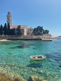 a small boat floating in clear blue water next to an island with a church on it