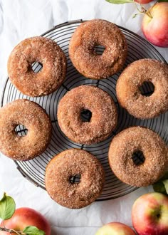 several donuts on a wire rack with apples in the background and leaves around them