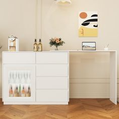 a white cabinet sitting on top of a wooden floor next to a vase with flowers