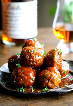 meatballs covered in sauce on a plate next to a glass of wine and a bottle