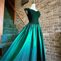 a green dress is on display in front of a brick wall and stair case,