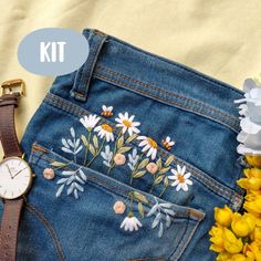 a pair of blue jean shorts with flowers on them next to a watch and yellow flowers