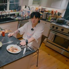 a woman sitting at a kitchen counter cutting food on a plate with a knife and fork