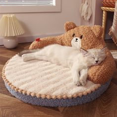 a white cat laying on top of a teddy bear bed next to a stuffed animal