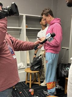 a man in a pink hoodie is holding a microphone and talking to another person