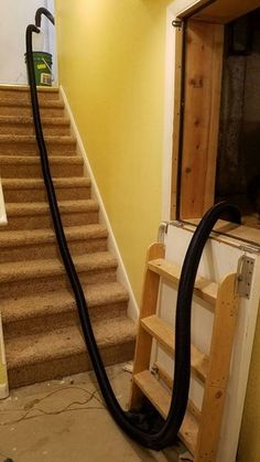 a black vacuum is on the ground in front of some stairs and a yellow wall