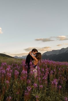 a man and woman kissing in a field of purple flowers with mountains in the background