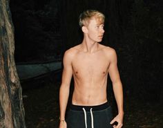 a shirtless young man standing in the woods at night with his hands on his hips