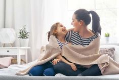 two women sitting on top of a bed with their arms around each other and smiling