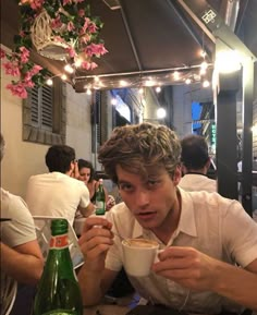 a young man sitting at a table with a cup of coffee in front of him