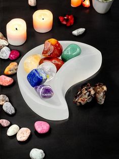 a bowl filled with lots of different colored rocks next to candles and some rocks on a table