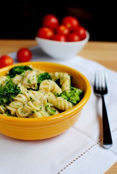 a yellow bowl filled with pasta and broccoli on top of a white napkin