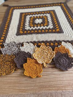 several crocheted flowers are laying on a wooden table next to a piece of cloth