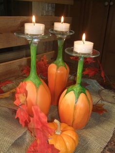 three glass pumpkins and two candles on a table