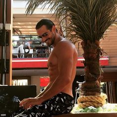 a shirtless man sitting on top of a table next to a potted plant