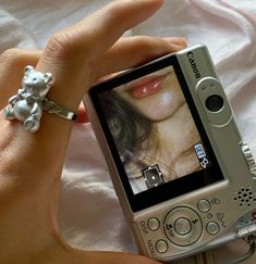 a person holding up a cell phone with a ring on it's thumb and the camera in their hand