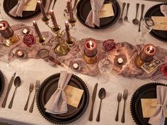 the table is set with black plates and silverware, napkins, and candles