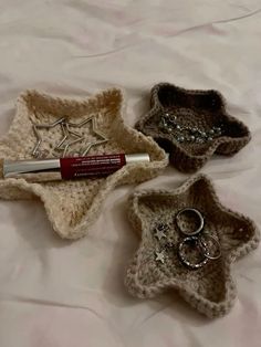 three small crocheted baskets with rings and lipstick on the bottom one has a pen in it