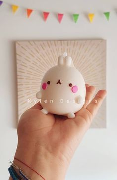 a hand holding a small white toy with pink eyes