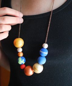 a woman wearing a black shirt holding a necklace with planets and stars on the beads