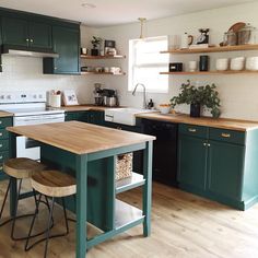 a kitchen with green cabinets and wooden counter tops, an island in between two stools